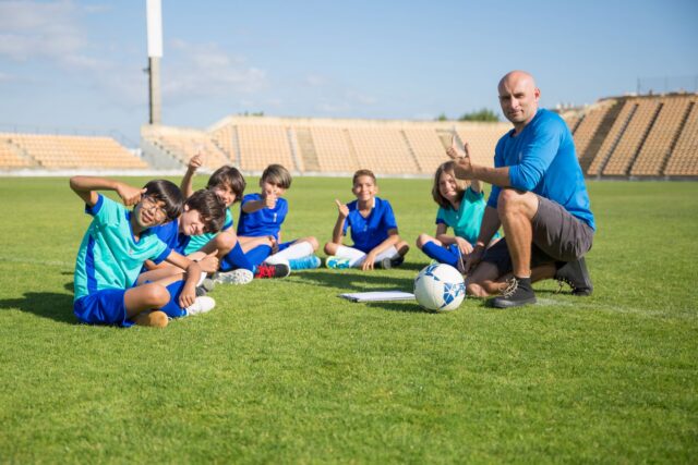 Antrenor care notează planul de pregătire pe un clipboard, lângă pista de atletism a unui stadion